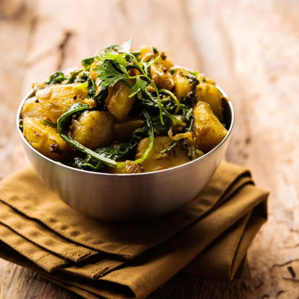 A metal bowl filled with Indian aloo palak, potatoes and spinach, on a brown napkin.